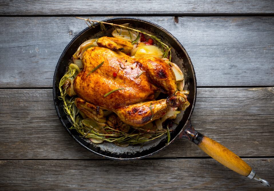 Roasted chicken in pan on the rustic wooden background. Selective focus.