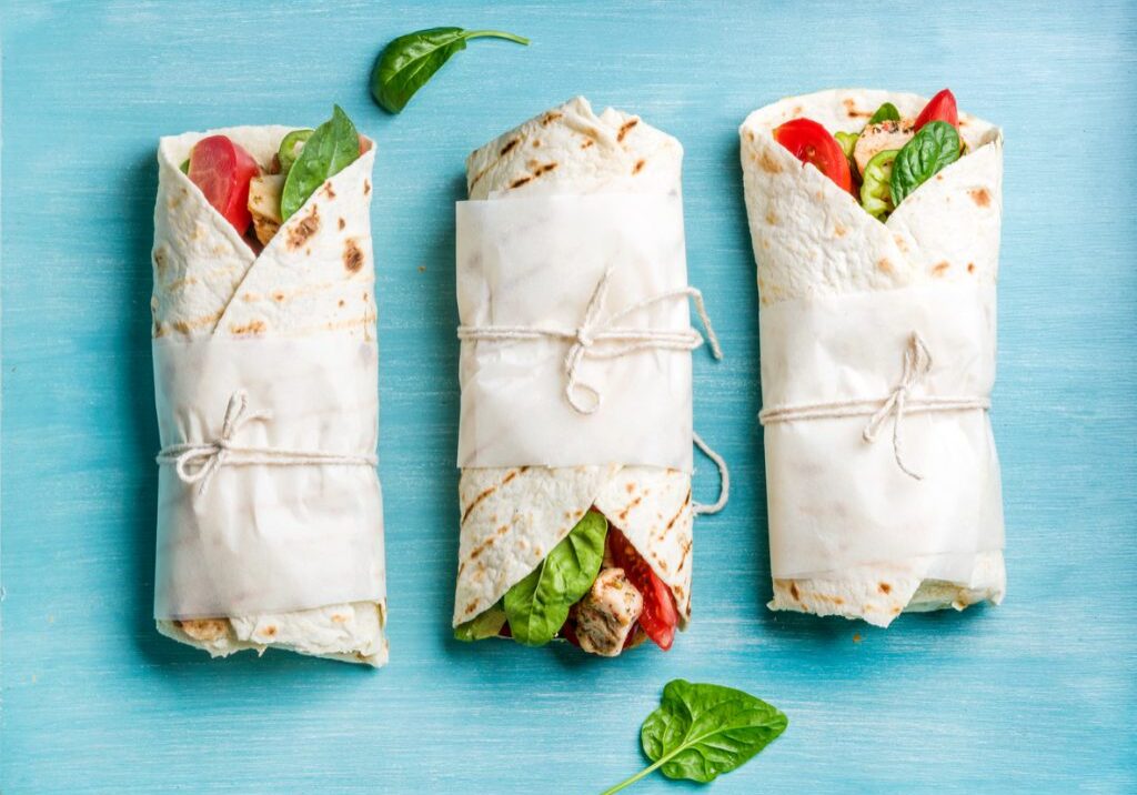 Healthy lunch snack. Tortilla wraps with grilled chicken fillet and fresh vegetables on blue painted wooden background. Top view